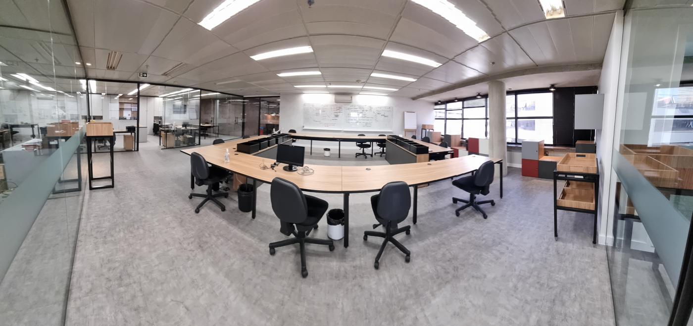 Open space corporativo amplo, com mesas em ilha e salas envidraçadas